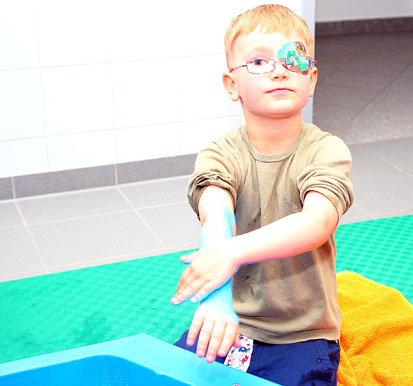 Ein kleiner Junge mit reibt seine Arme mit blauer Seifenfarbe ein.